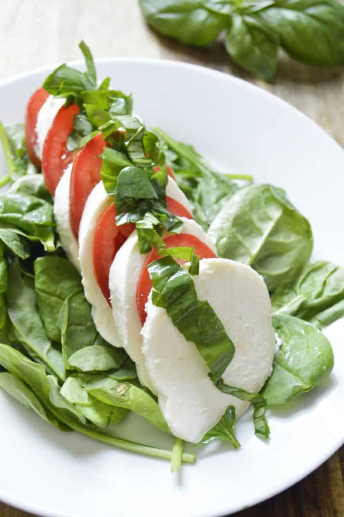 Sliced tomatoes and mozzarella on a bed of spinach, topped with fresh basil.