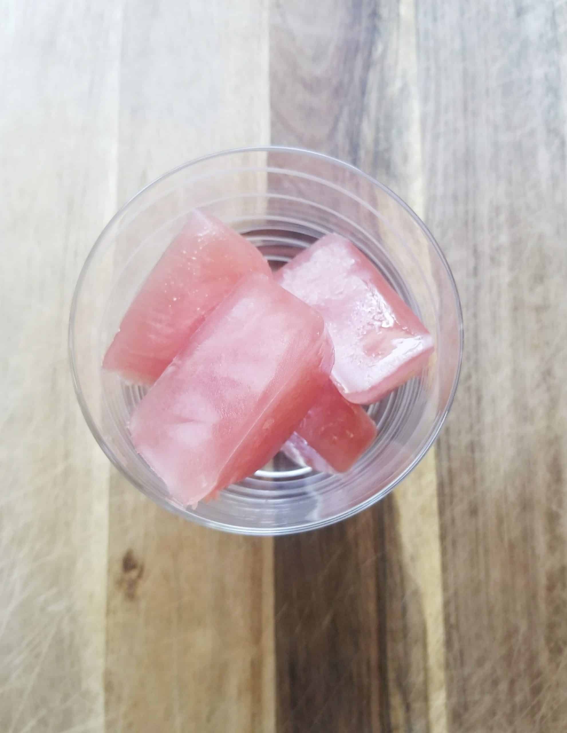 Overhead photo of cranberry ice cubes in a glass with a wood background.