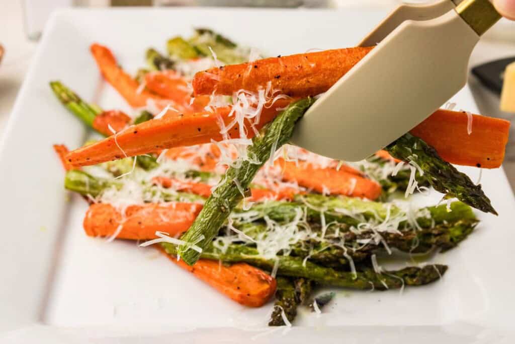 Serving roasted asparagus and carrots with Parmesan from a white platter.