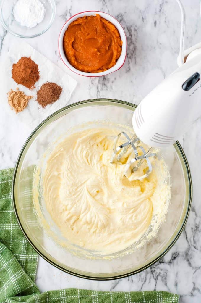 Bread Batter with electric mixer in a bowl with spices and pumpkin purée beside it.