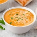 Pumpkin soup in a white bowl with cream on top and fresh parsley sprinkled on top.
