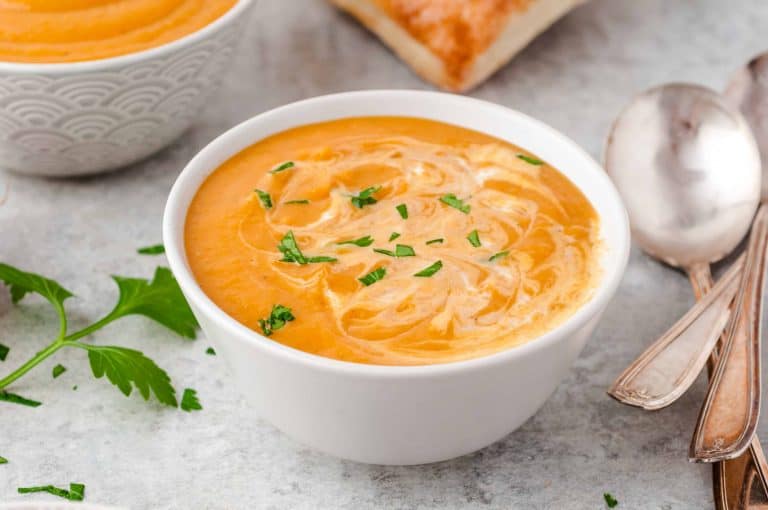 Pumpkin soup in a white bowl with cream on top and fresh parsley sprinkled on top.