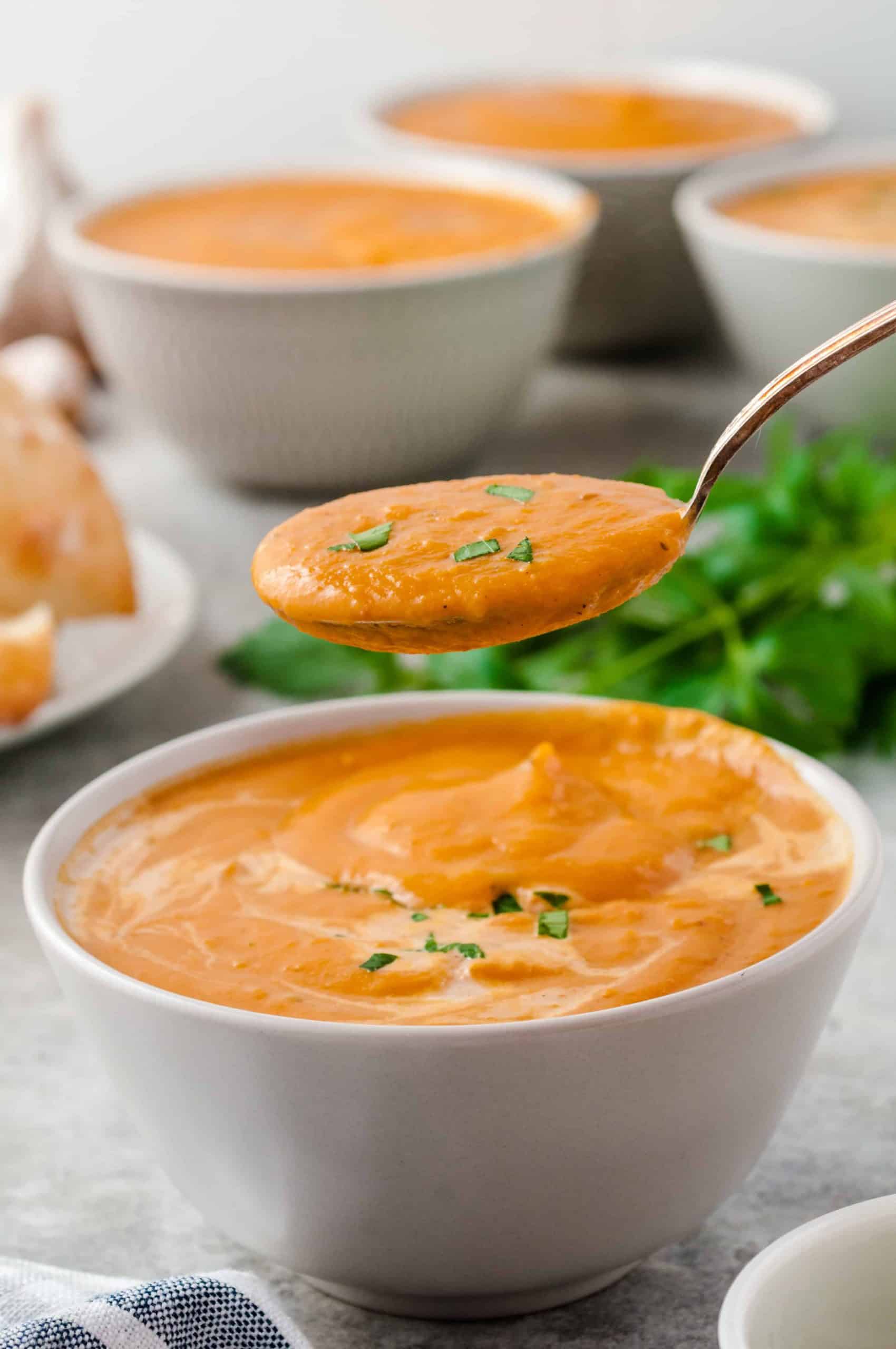 Closeup of spoonful of pumpkin soup with 3 bowls of pumpkin soup in the back.