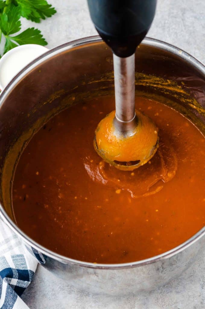 Immersion blender in a pot with pumpkin soup.