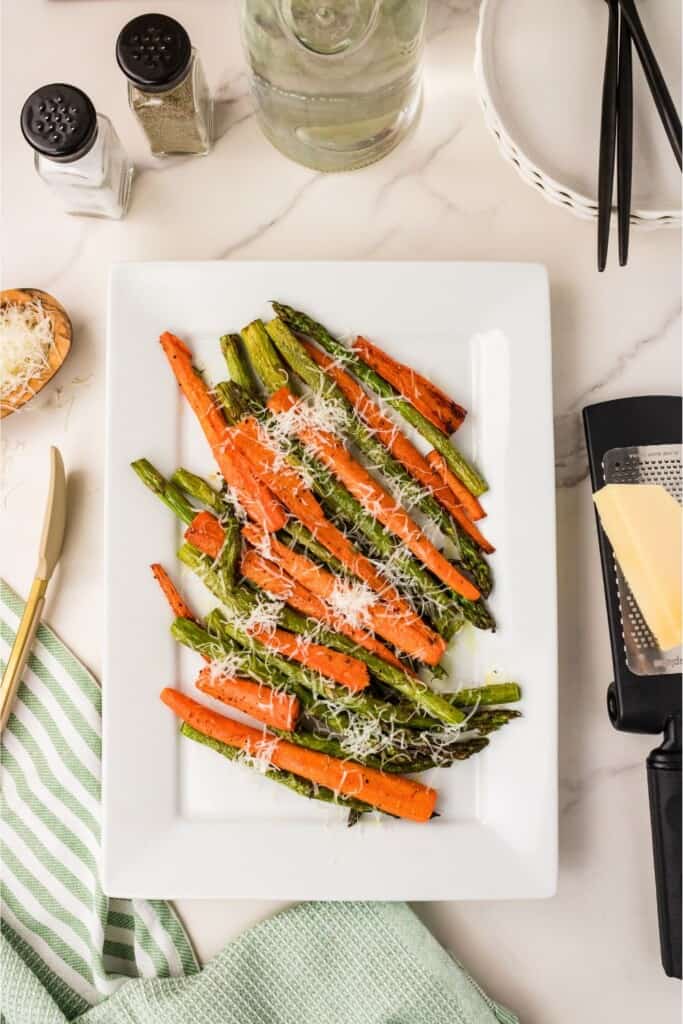 Roasted asparagus and carrots with Parmesan on a white plate, freshly grated Parmesan on top.