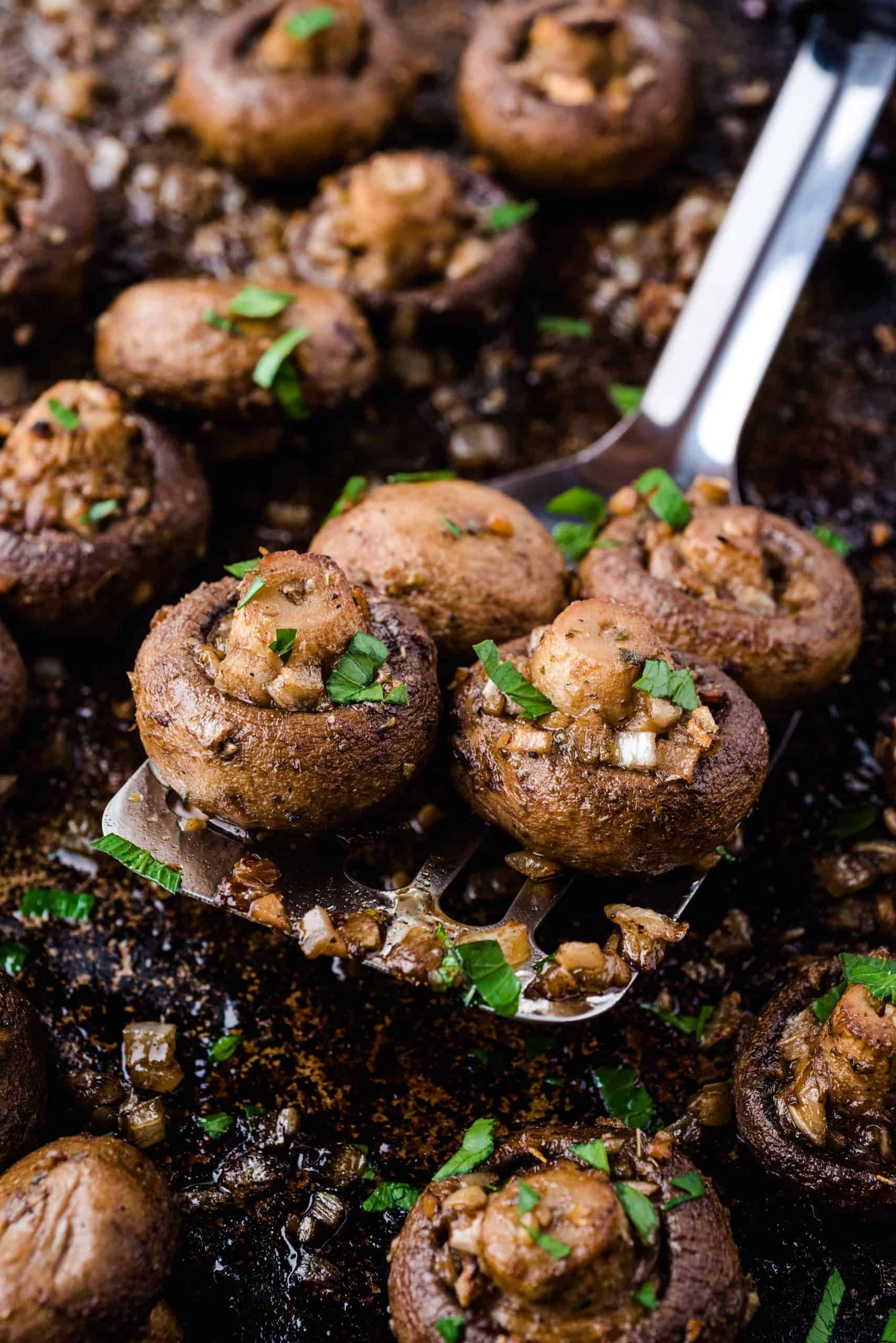 Oven Roasted Mushrooms on a baking sheet with some on top of a spatula with butter sauce, parsley and garlic.