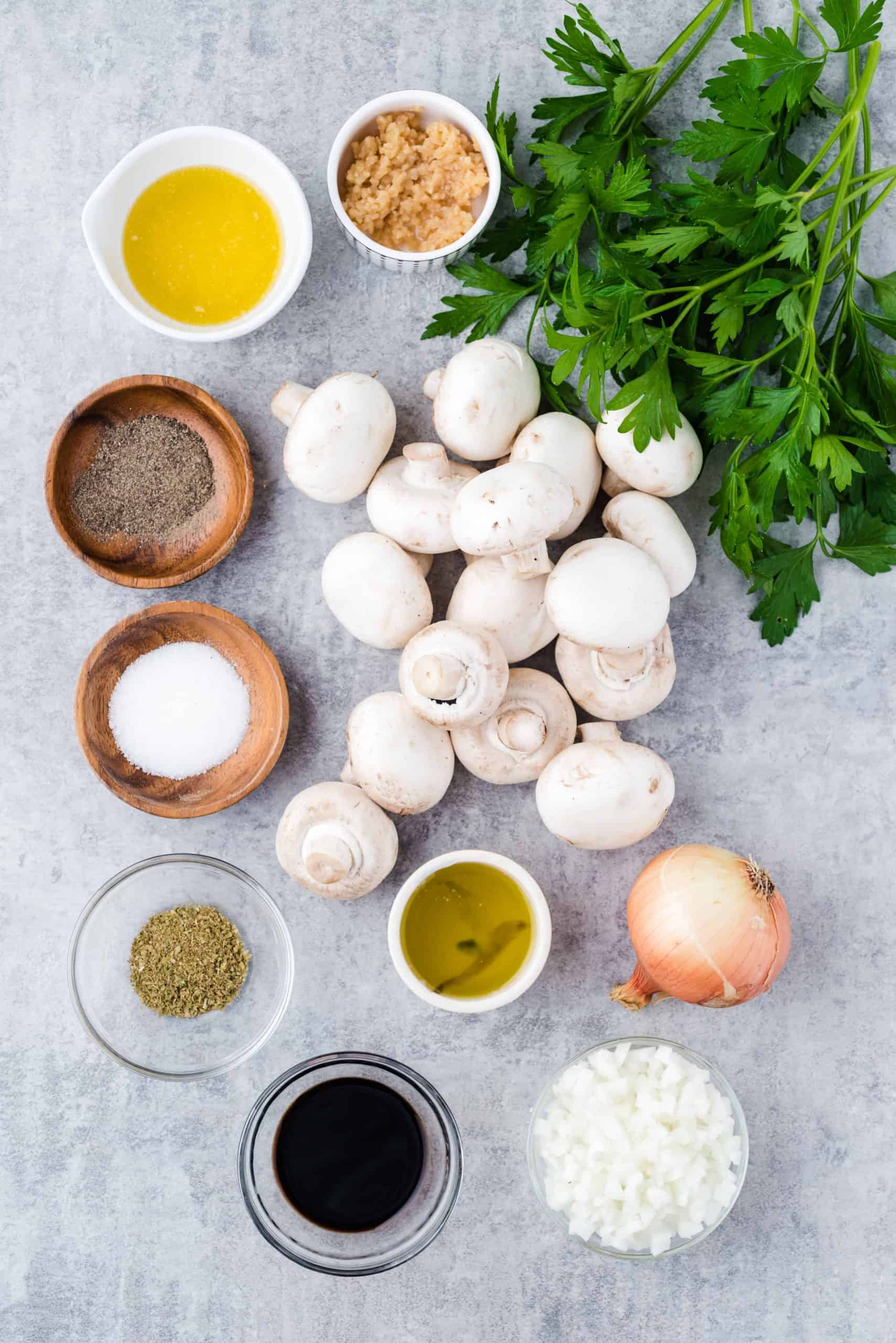 White mushrooms, parsley and small measuring cups with other ingredients for mushroom recipe.
