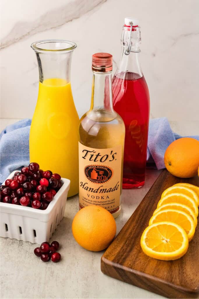 Ingredients for vodka cranberry orange juice cocktail including Tito's vodka, cranberry juice, orange juice, and fresh oranges