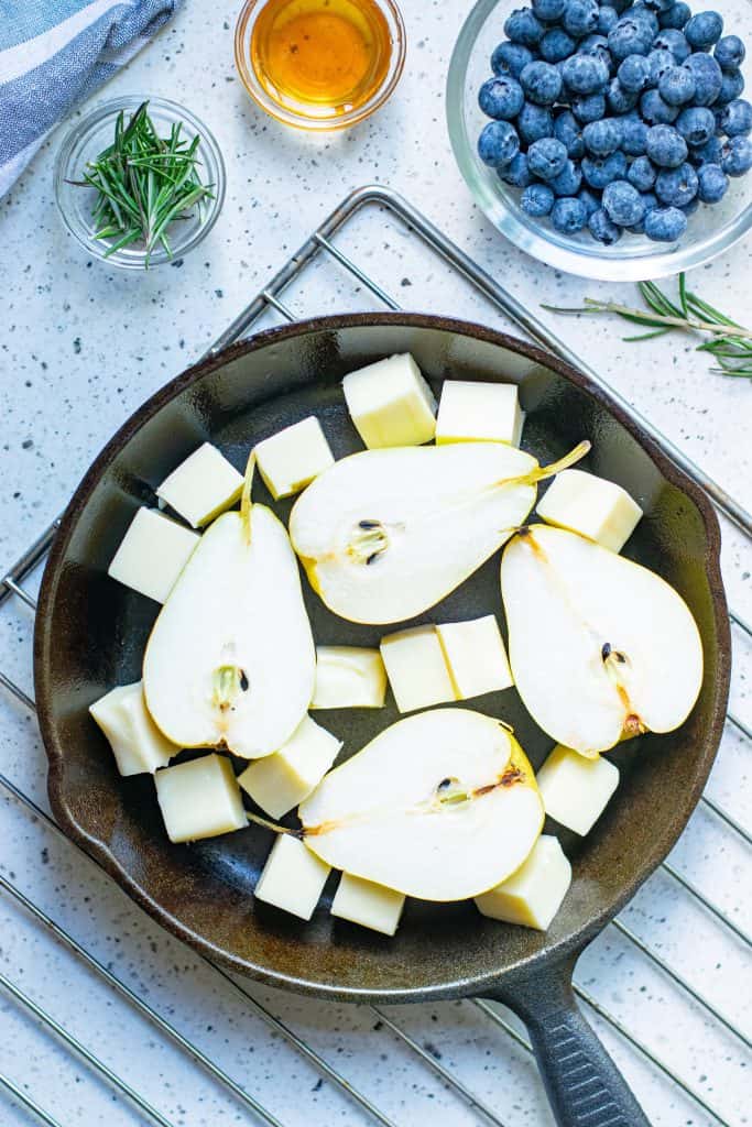 Overhead view of pear halves with cubes of mozzarella around it in a cast iron skillet on a wire baking rack.