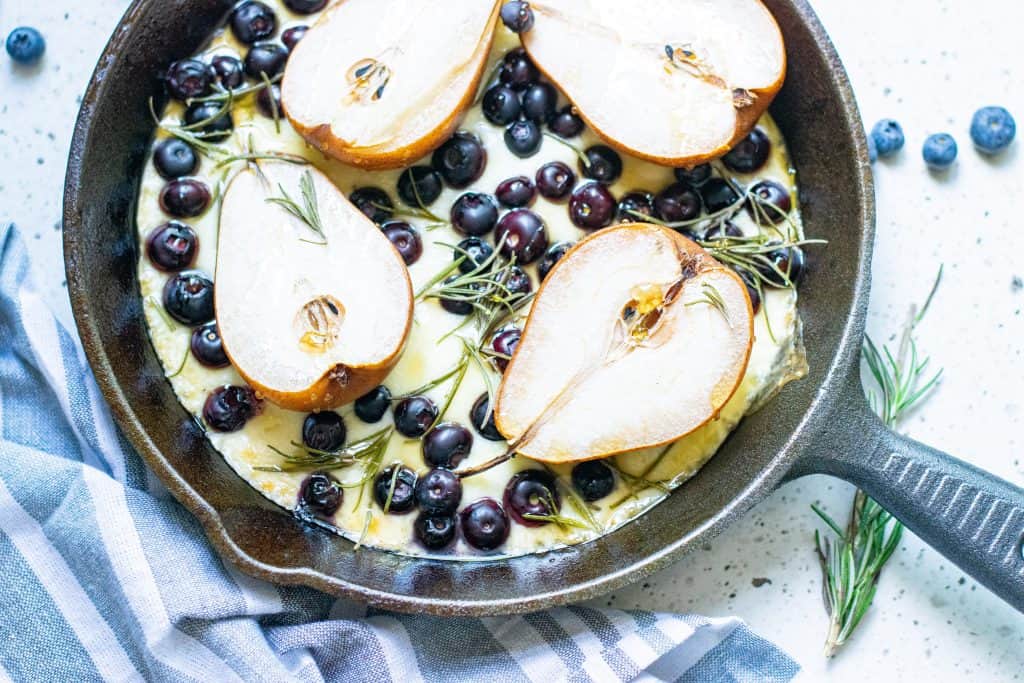 Pears, blueberries, mozzarella cheese and rosemary in a black iron skillet.