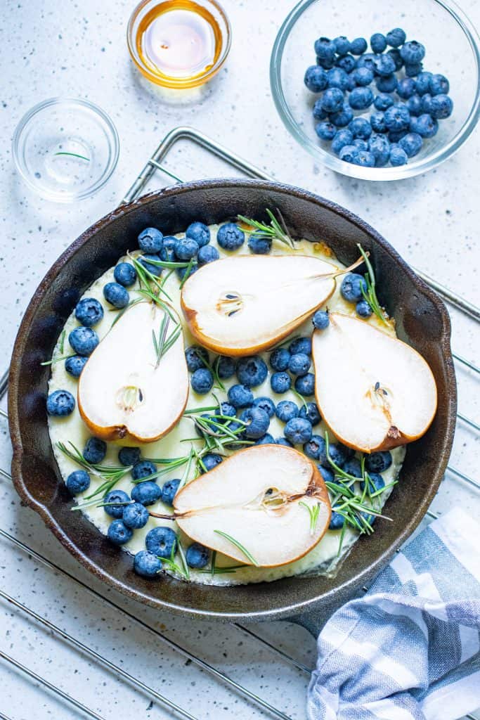 Pears, blueberries, melted cheese and fresh rosemary in a black iron skillet.