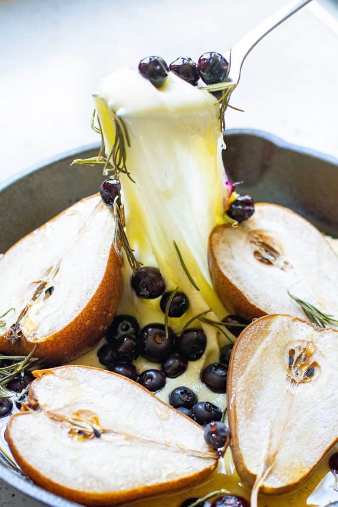 Mozzarella cheese and blueberries being pulled out of a black iron skillet that has baked pears in it.