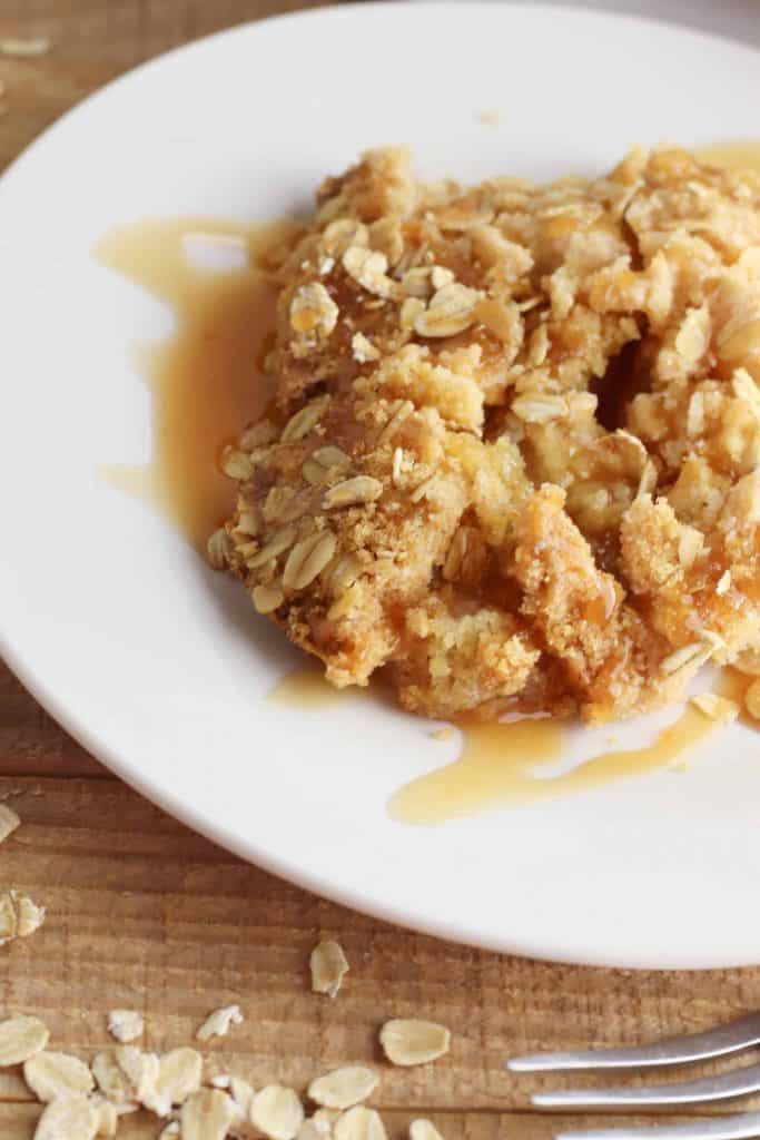 Easy Apple Dump Cake in a white bowl with caramel drizzled on top.