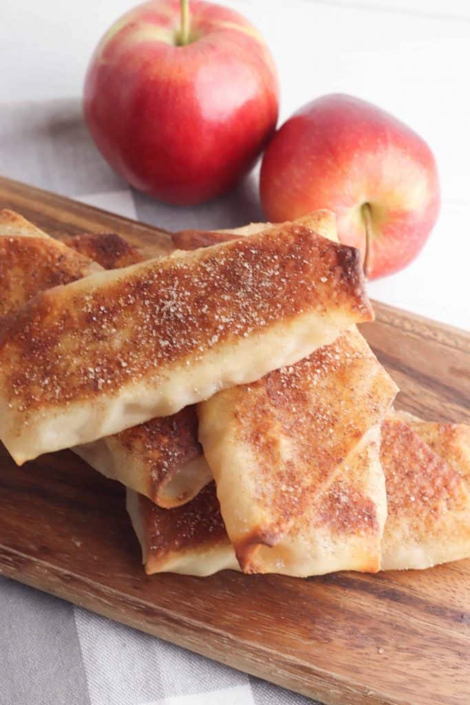 Apple Pie Egg Rolls on a wood cutting board with apples in the background.