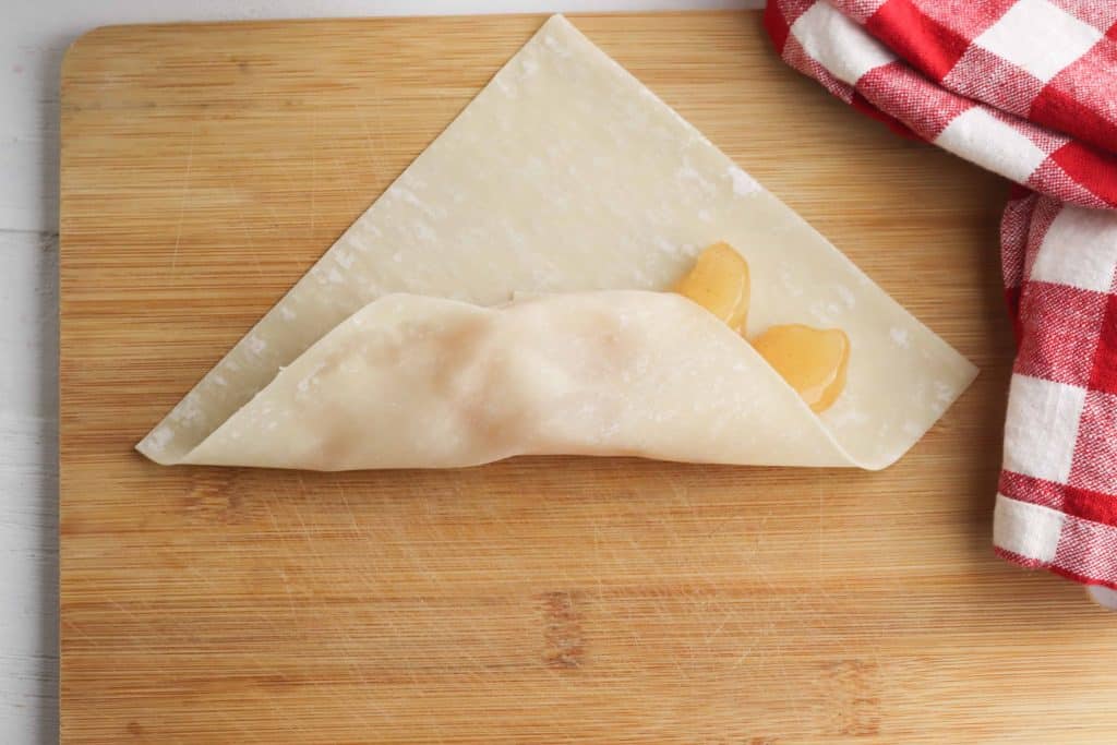 Egg roll wrapper folder over apples on a cutting board.