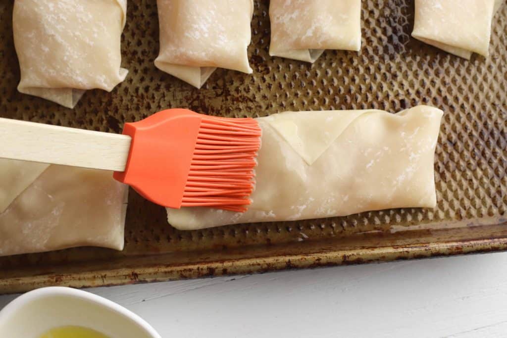 Vegetable oil being brushed on top of egg rolls with a basting brush.