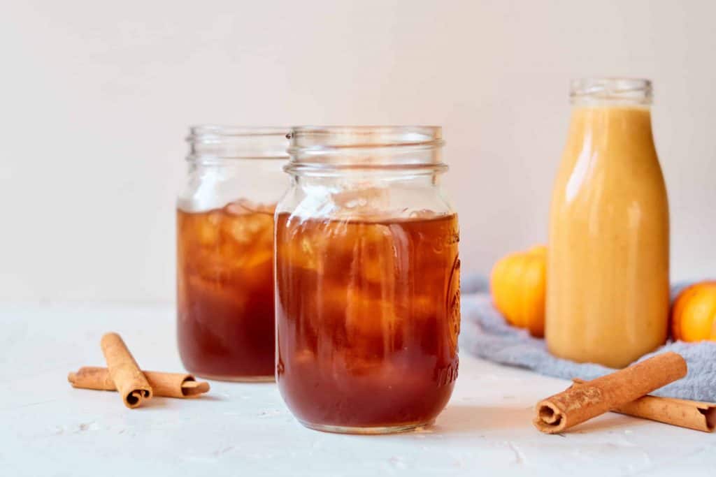 Iced coffee with vegan pumpkin spice creamer in the background