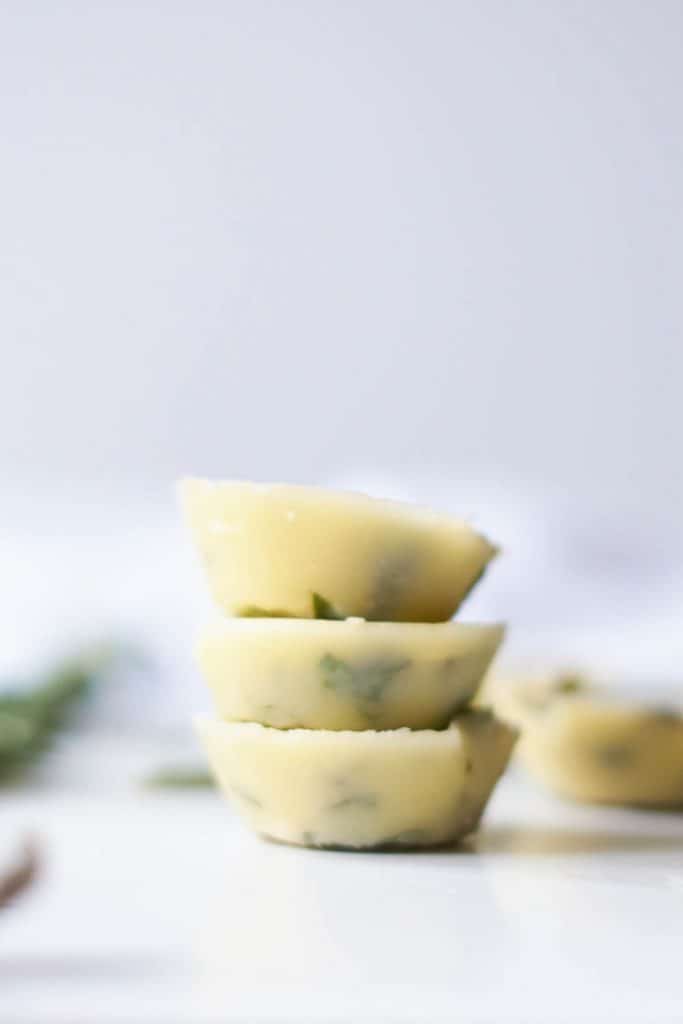 Stacked herbed butter on a white background with fresh herbs and additional butter in the background.