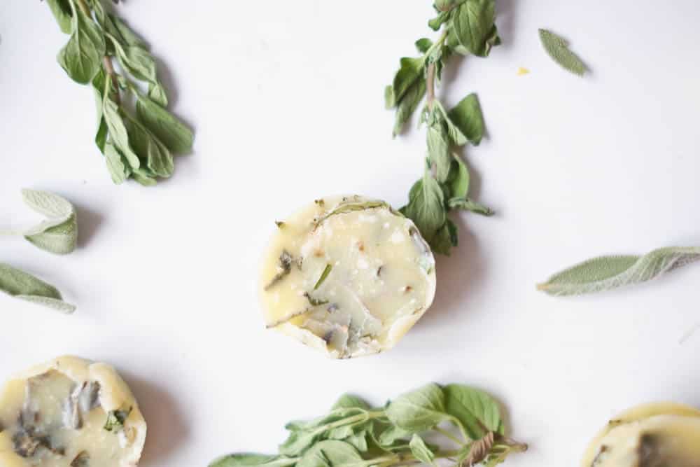 Italian herbed butter on a qhite background with fresh herbs around it.