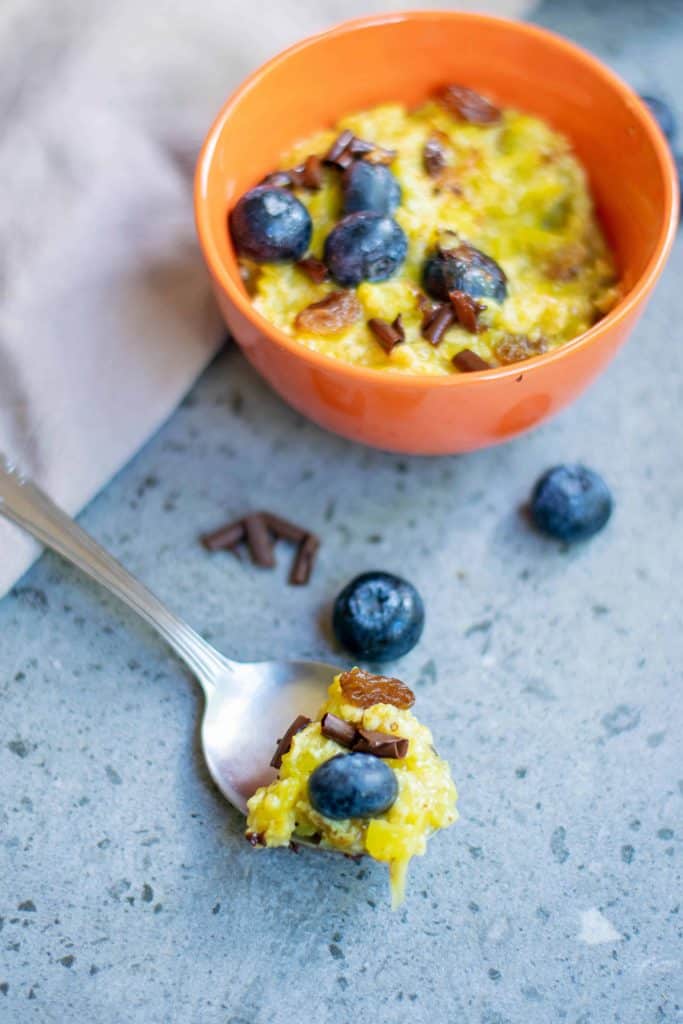 Pumpkin Oatmeal in an orange bowl with a spoonful of pumpkin oatmeal on a spoon with blueberries.