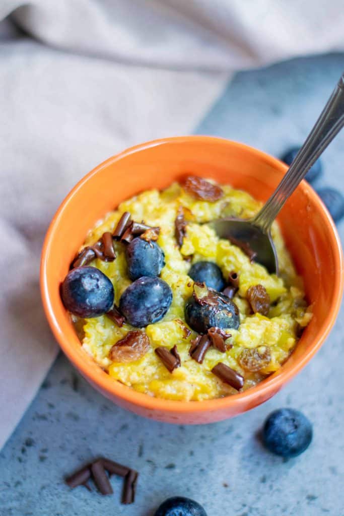 Pumpkin oatmeal topped with blueberries in an orange bowl with a spoon in it.