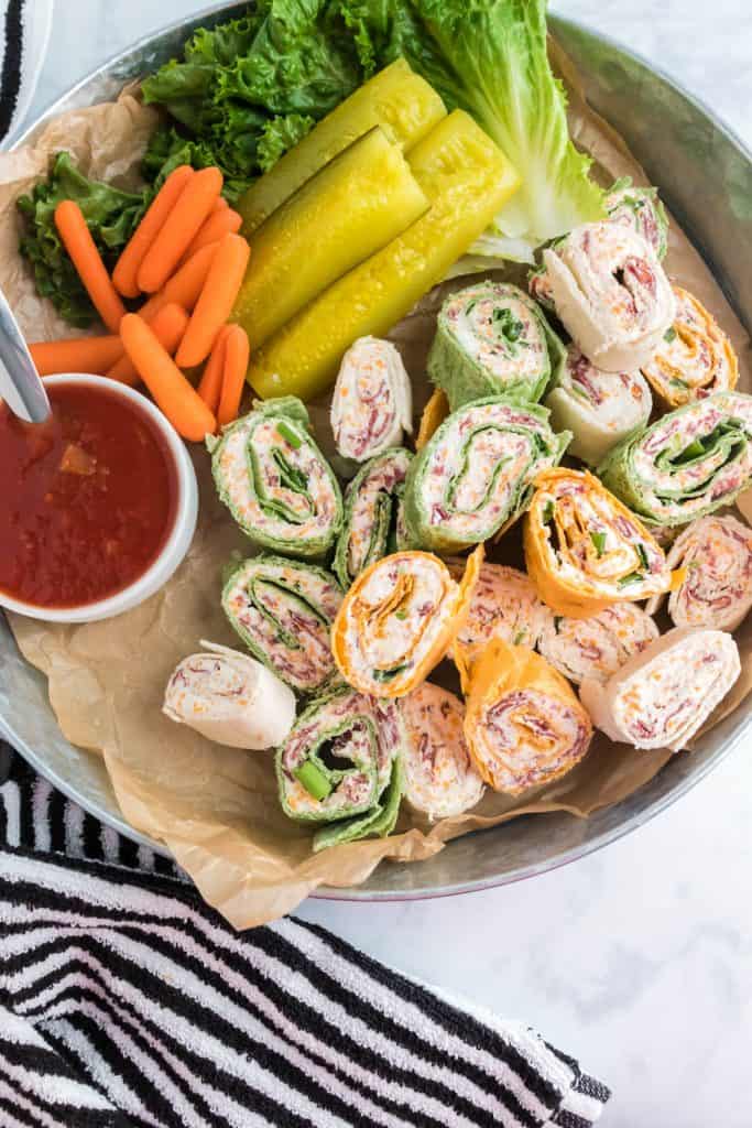 Easy Party Pinwheels on a platter with pickles, carrots, salsa and green leafy lettuce