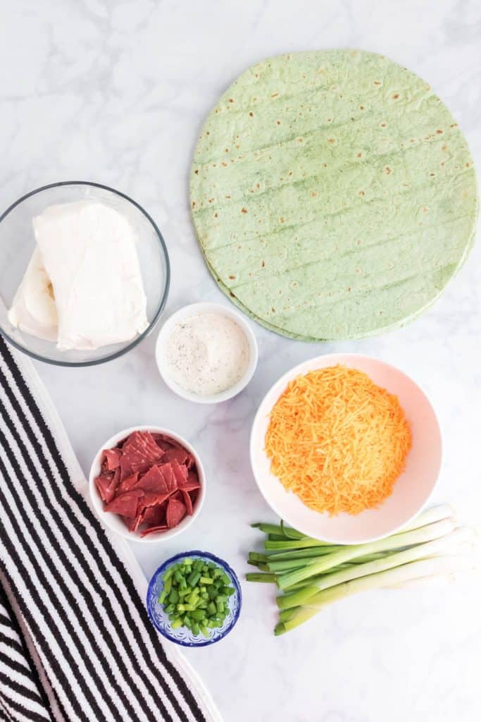 \Spinach Tortillas, cheddar cheese, dried beef, cream cheese and green onions on a white counter top