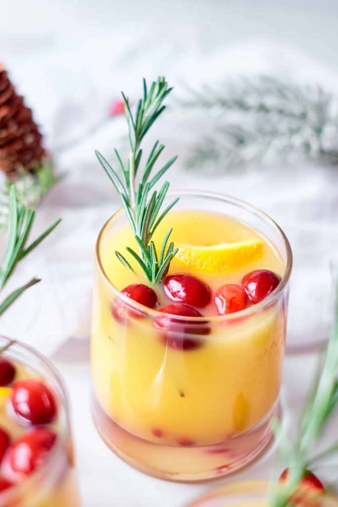 Single orange mocktail with sprig of fresh rosemary and cranberries