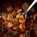A ladle with beef stew over a dutch oven filled with the beef stew.