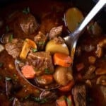 A ladle with beef stew over a dutch oven filled with the beef stew.