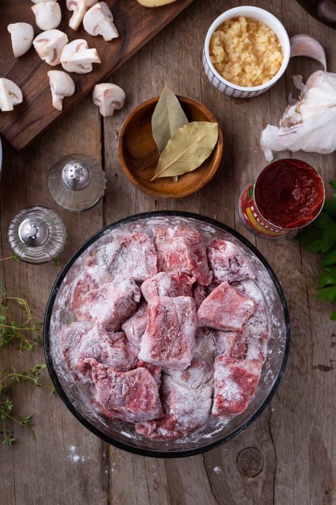 Stew beef coated with flour in a glass mixing bowl.