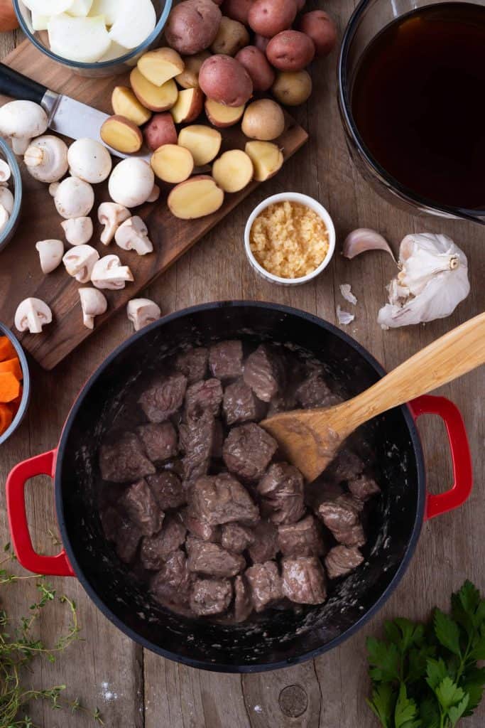 Browned beef in a Dutch oven with a wooden spoon in the pot.
