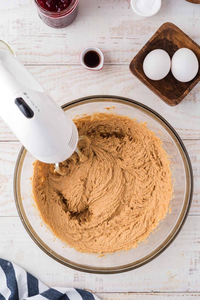 Peanut butter cookie dough with electric mixer in a glass bowl.