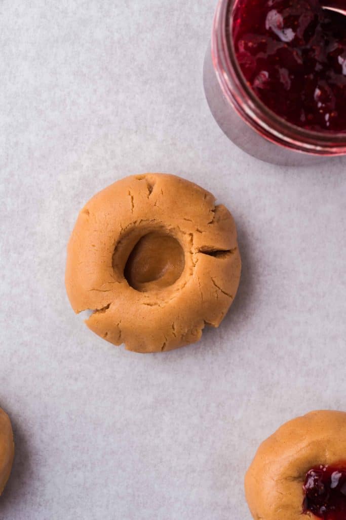 Peanut butter cookie, unbaked with thumb print in the center.