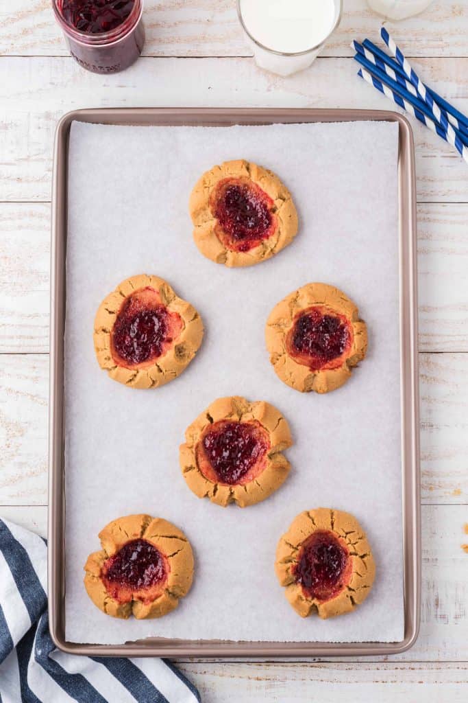 Baked peanut butter and jam cookies on parchment lined baking sheet.