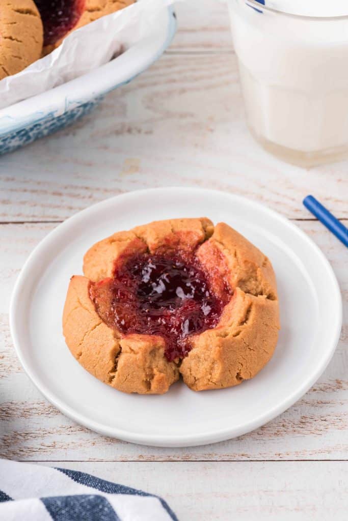 Single peanut butter and strawberry jelly cookie on a white plate.