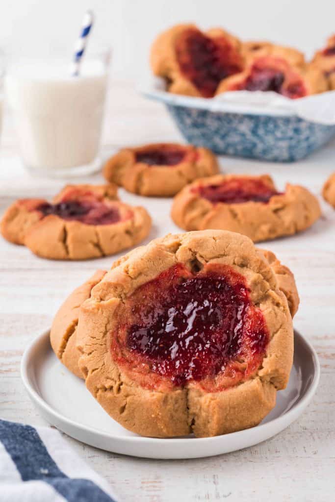 Close up of Peanut Butter and Jam Cookie with other cookies in the background and a glass of milk with a straw.