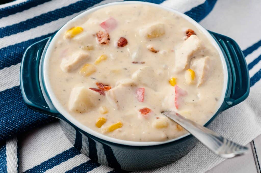 Closeup of corn chowder in a blue enamel bowl with a spoon in it.