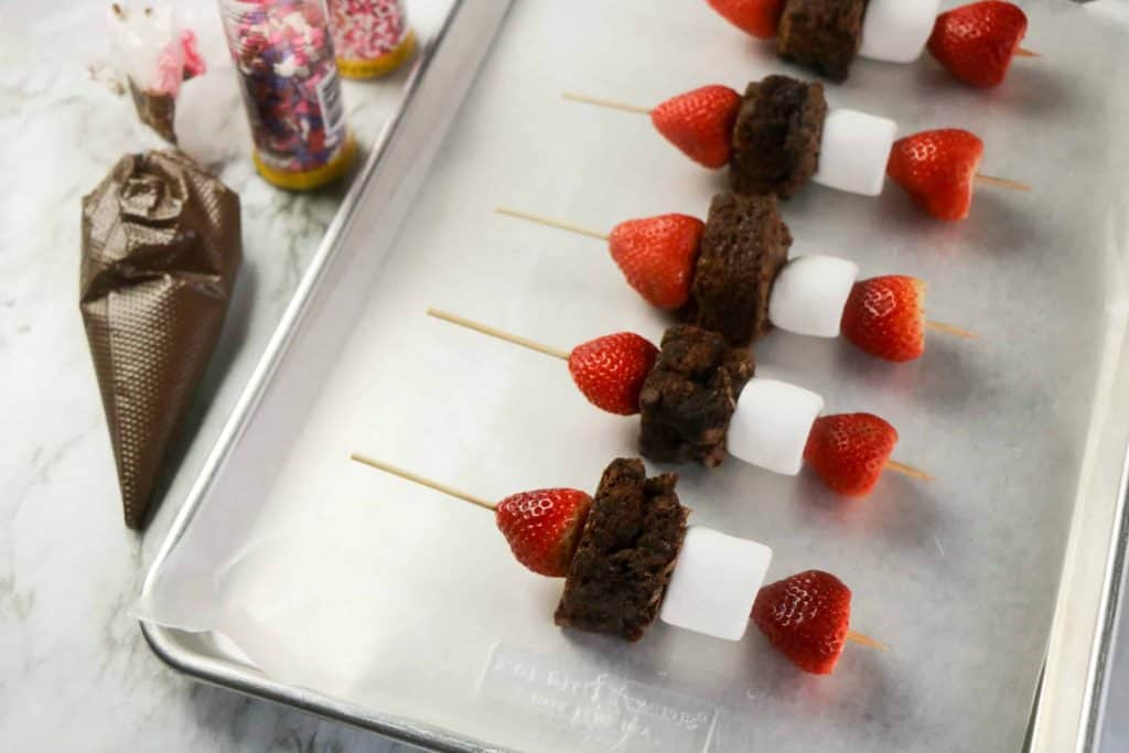 Baking pan lined with wax paper with dessert sticks on it.