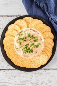 Overhead view of crack chicken dip surrounded with crackers on a black platter.