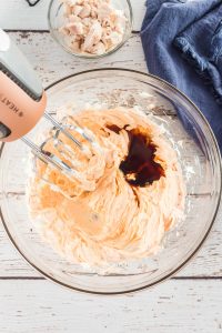 Cream cheese with spices and soy sauce in a glass mixing bowl with a hand mixer in it blending the ingredients.