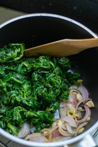 Spinach bin a sauce pan with red onion and garlic.