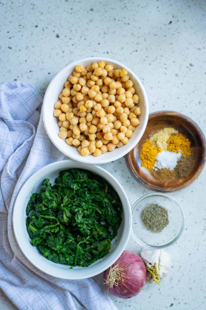 Overhead shot of bowl of chickpeas, bowl of frozen spinach and spices.