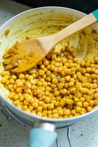 Curried chickpeas in a skillet with a wooden spoon in them.