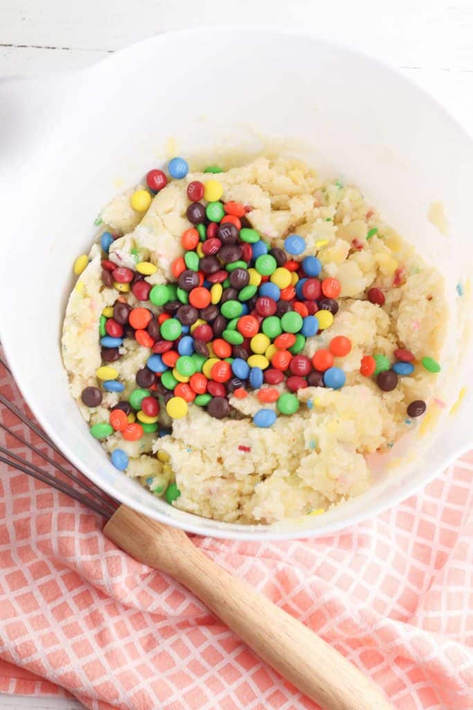 Overhead photo of cookie dough in a white bowl with mini M&Ms on top of the dough.
