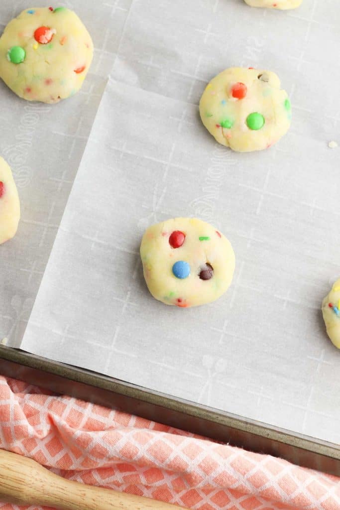 Balls of gluten free Funfetti cookie dough on a parchment lined baking sheet.