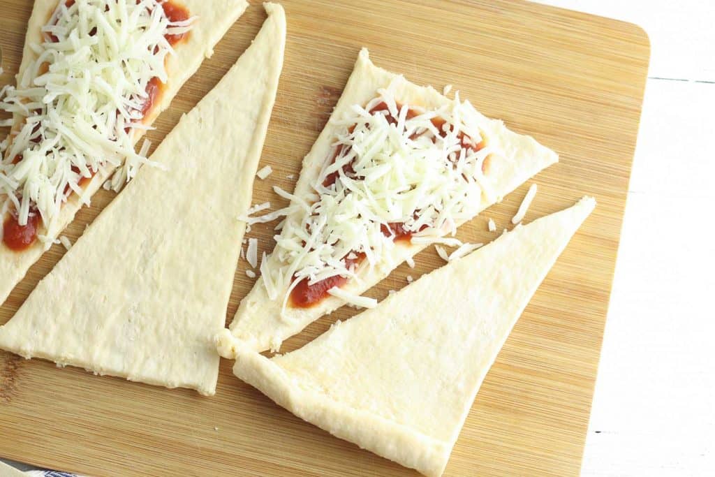 Cheese and sauce on top of Crescent Roll dough on a cutting board.