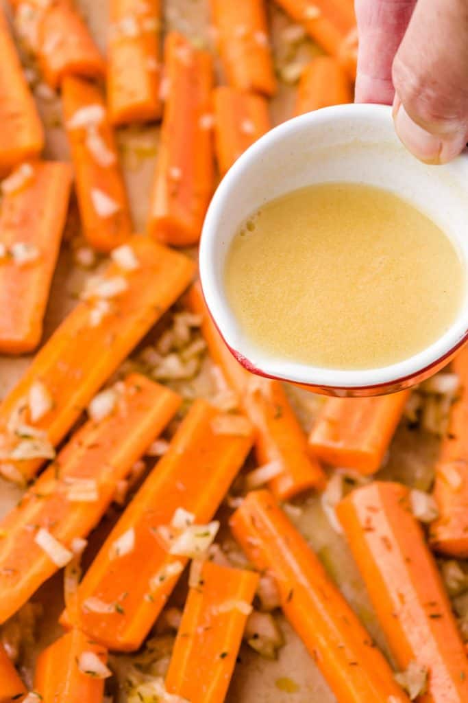 Closeup of small bowl of vegetable bouillon broth being ready to be poured onto carrots.