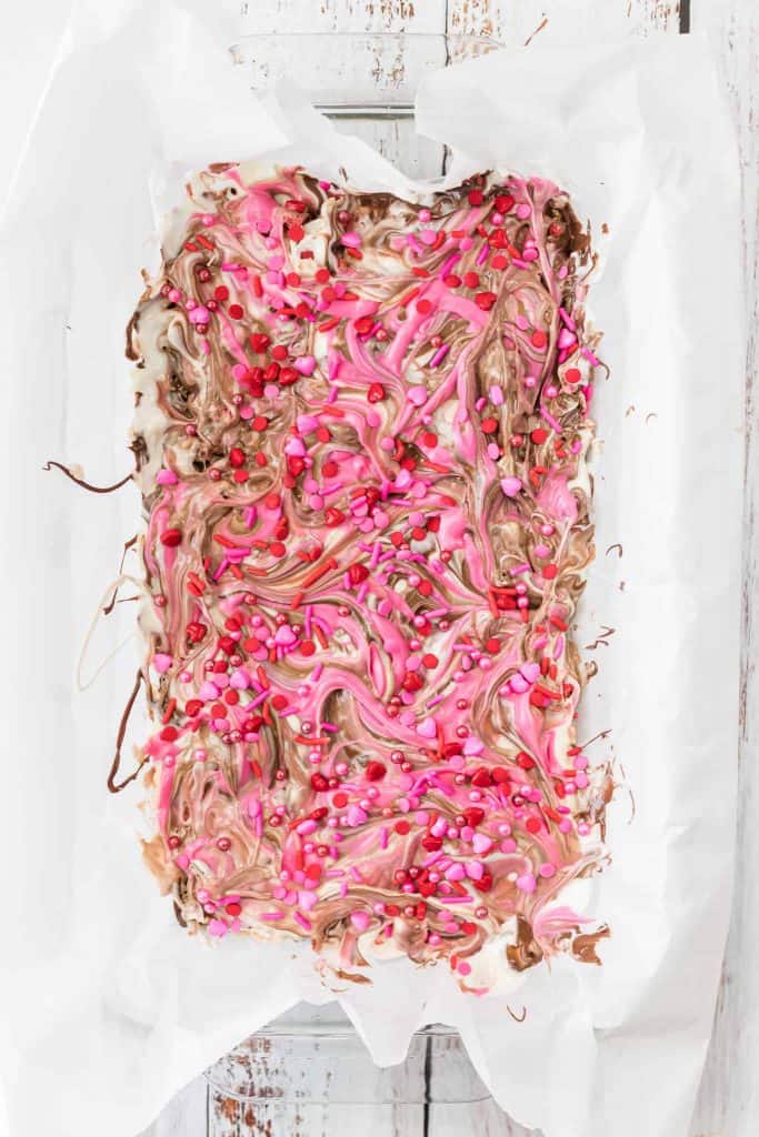 Valentine's Day themed swirled candy bark on parchment paper on a white wood background.