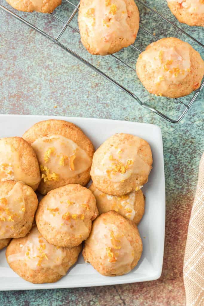 Carrot Cookies with orange glaze on white platter and on a wire rack.